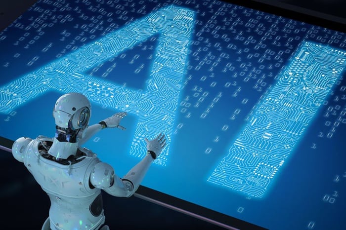 A humanoid robot in front of a digital screen with AI superimposed on it.