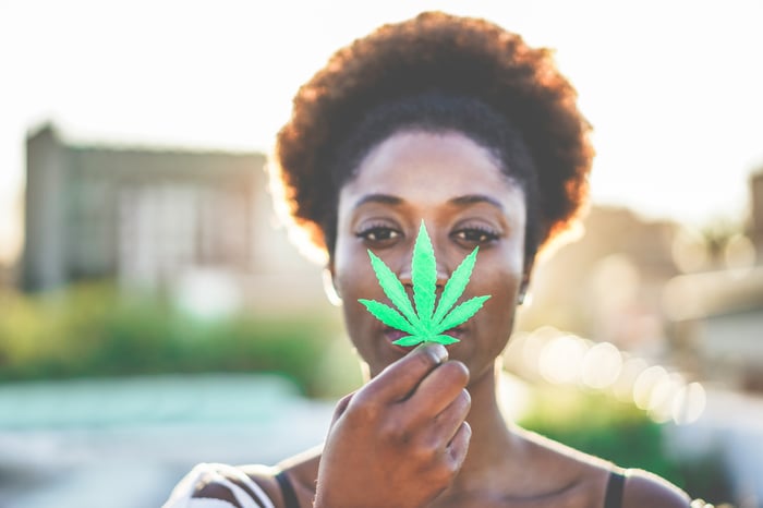 A person holding a cannabis leaf in front of their face.