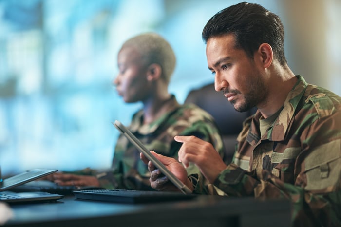 Person in the military using a tablet computer while sitting beside a peer.