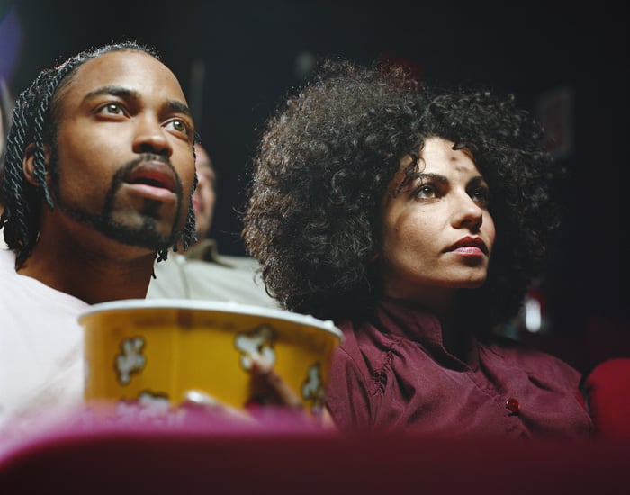 Two people watching a movie at a theater, holding a popcorn bucket.