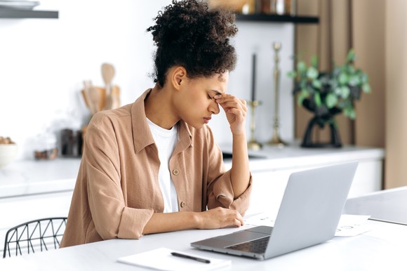 Unhappy person works on a laptop at a dining table.