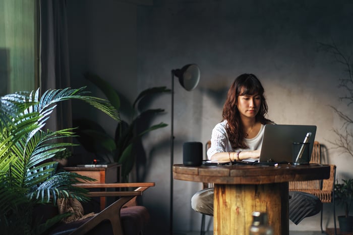 A person working on a laptop while sitting at a rustic table in their den.