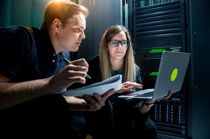 Two engineers working on a laptop in a data center.