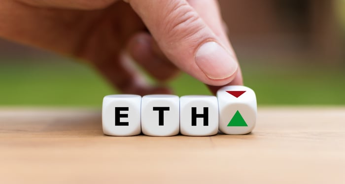 A row of dice spell out the ETH ticker. A hand is moving the last die from a red arrow pointing down to a green one pointing up.