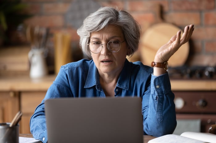 A person shrugs and scowls at their laptop screen.