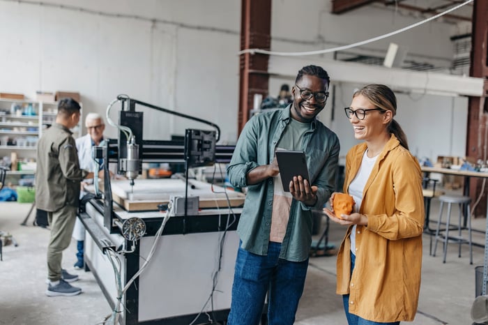 Two people in an industrial space occupied by a 3D printer.