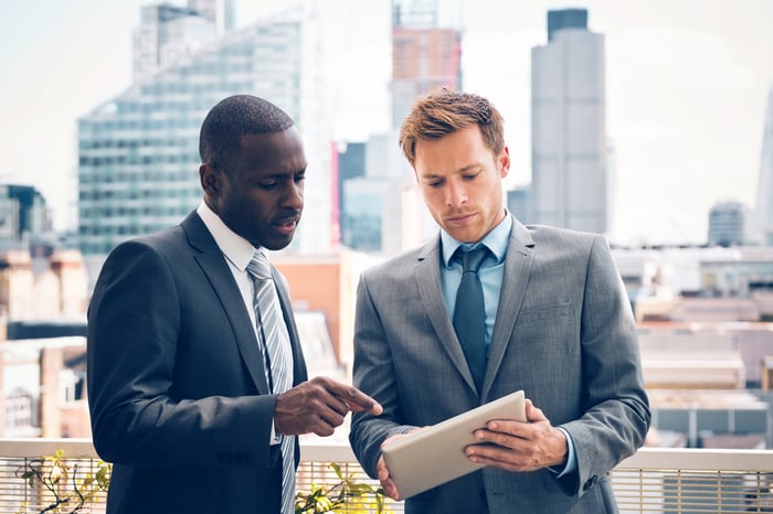Two people outside wearing suits and looking at a tablet.