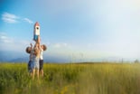 children lift a toy rocket in a field.