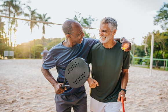 Two people holding rackets or paddles while standing on a sandy court.