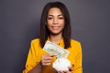 22_03_07 A person putting a 100 dollar bill into a piggy bank _GettyImages-1203959263