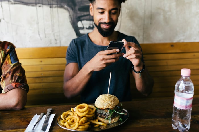 Person photographing a plate with onion rings and a burger on it. 