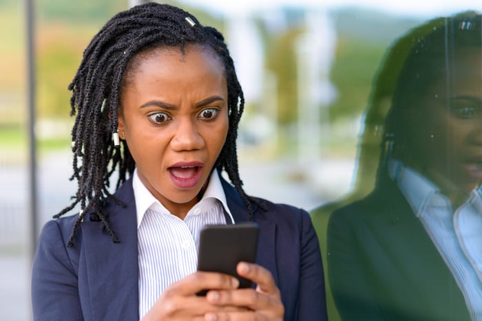 A person looking at their cell phone in a surprised manner.