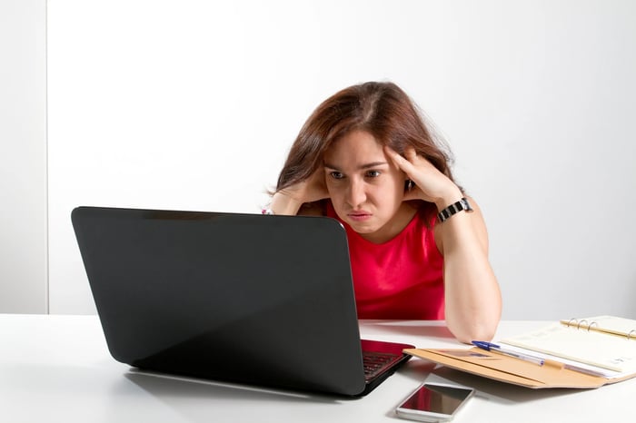 A person sits and stares at a laptop while looking frustrated. 