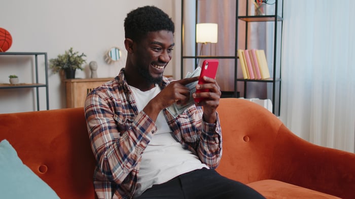 Person on a couch smiling while using a smartphone.