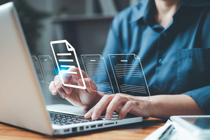 Person using laptop with digital document icons floating above, symbolizing online file management.