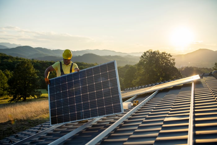 Worker laying down solar panel array at twilight. 