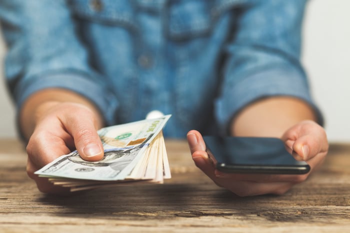 A person holding a phone in one hand and cash in the other. 
