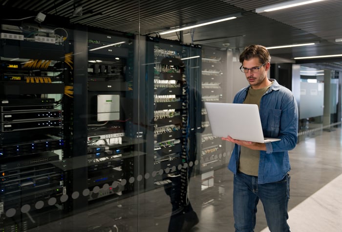 Someone holding laptop while inspecting server racks in a modern data center.