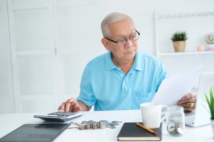 A person holding a document and hovering over a calculator.