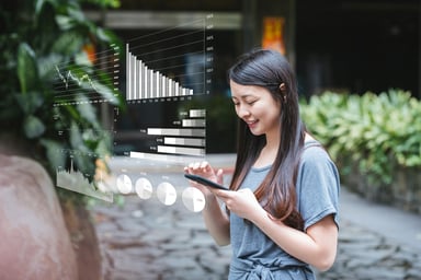 A person smiles while looking at their phone, which is emitting a digital display of investing graphs and charts.