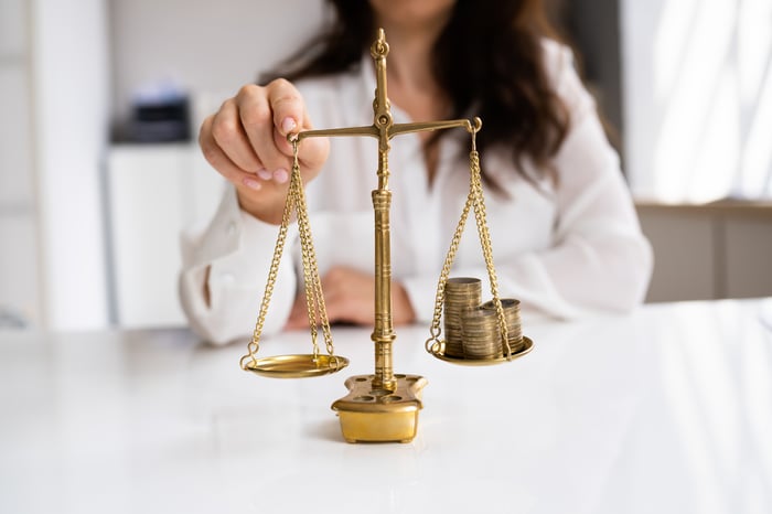A person tipping a scale that holds coins on one side and nothing on the other.