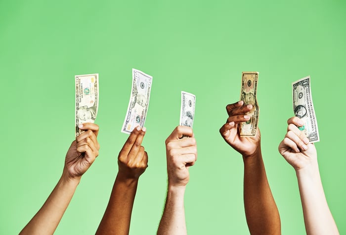 Five hands holding U.S. currency in the air.