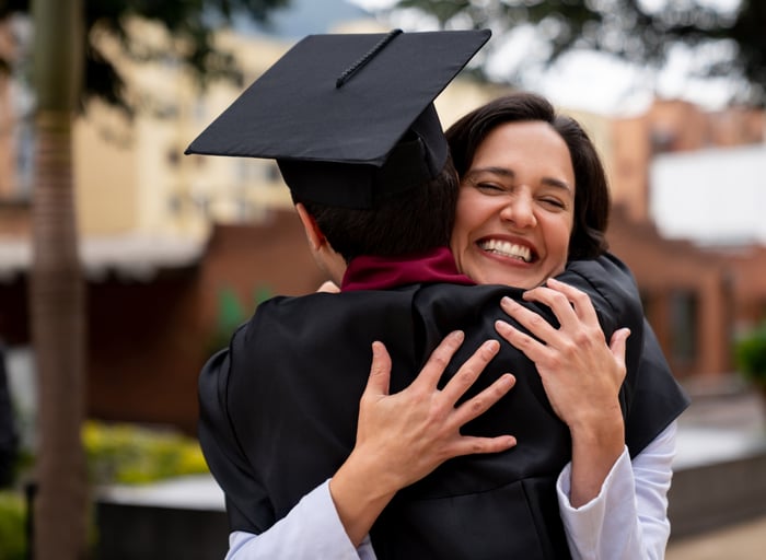 Person hugging a graduate in cap and gown during a joyful celebration.