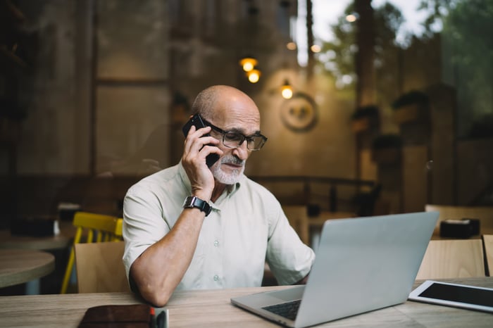A person talking on a phone, looking at a laptop.