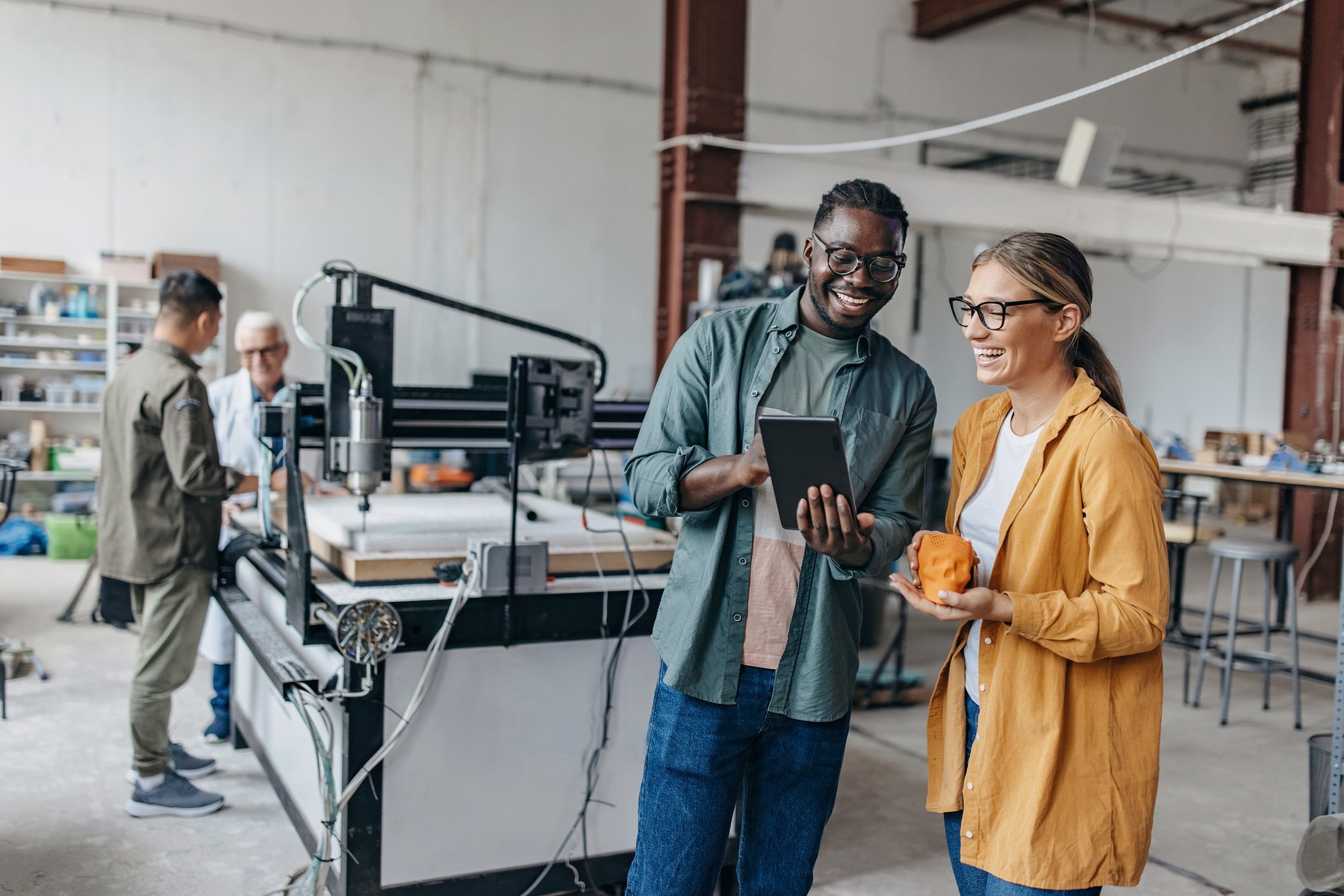 Two people in an industrial space occupied by a 3D printer