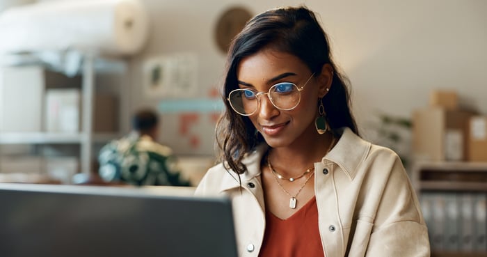 A person smiles while sitting in front of a laptop computer.