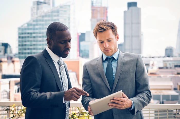 Two people in suits looking at a tablet.