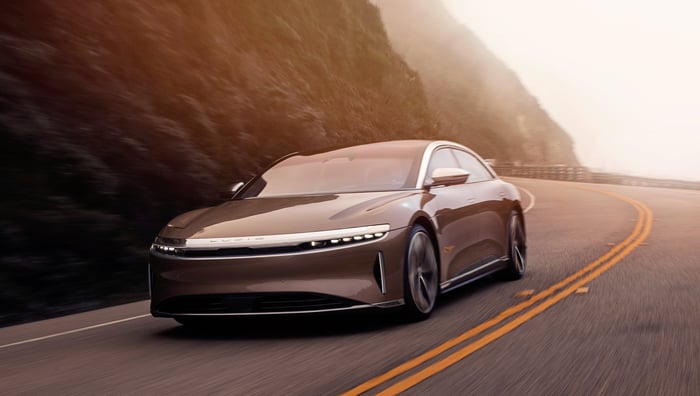An all-electric Lucid Air sedan driving on a one-lane mountain road. 