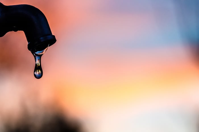 A water droplet falling from an outdoor spigot, with daylight beginning to emerge on the horizon.