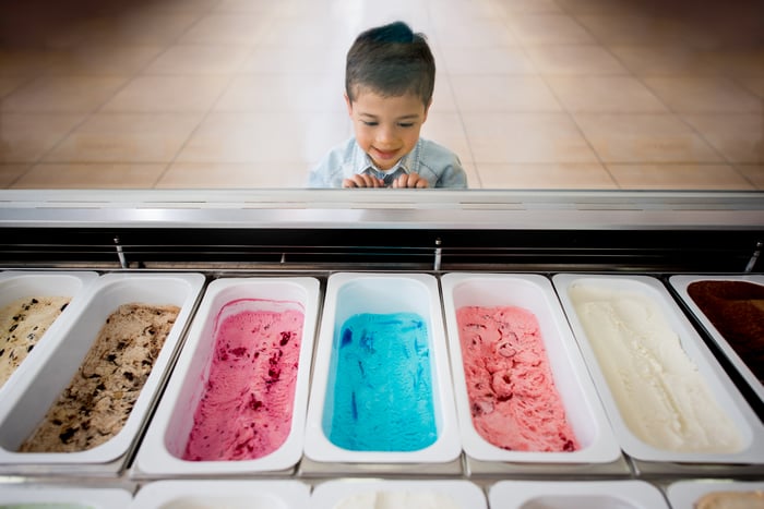 A child looks at a variety of ice cream flavors sitting in white tubs behind the glass of an ice cream shop's display case.