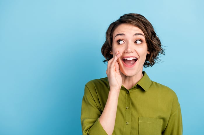 Person cupping hand to mouth in excitement as they pass along some hot information.