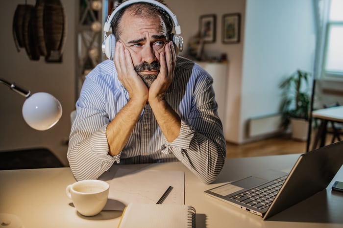 A person wearing headphones frowns at an unseen laptop computer screen.