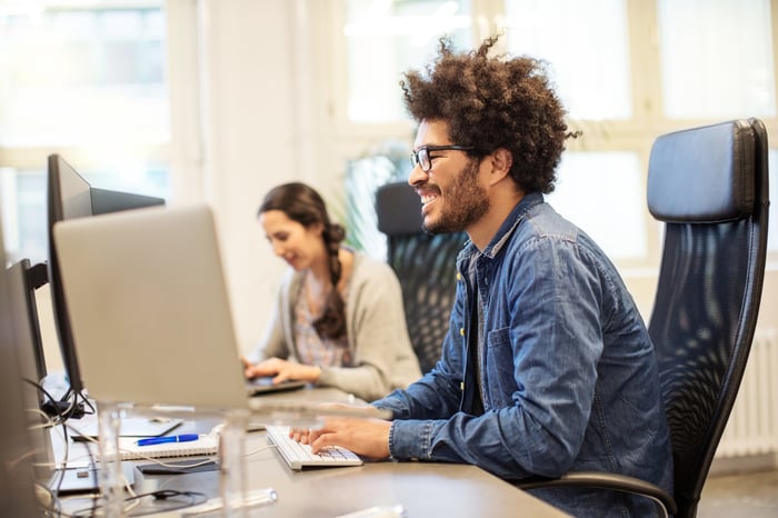 A smiling human interacts with a personal computer.