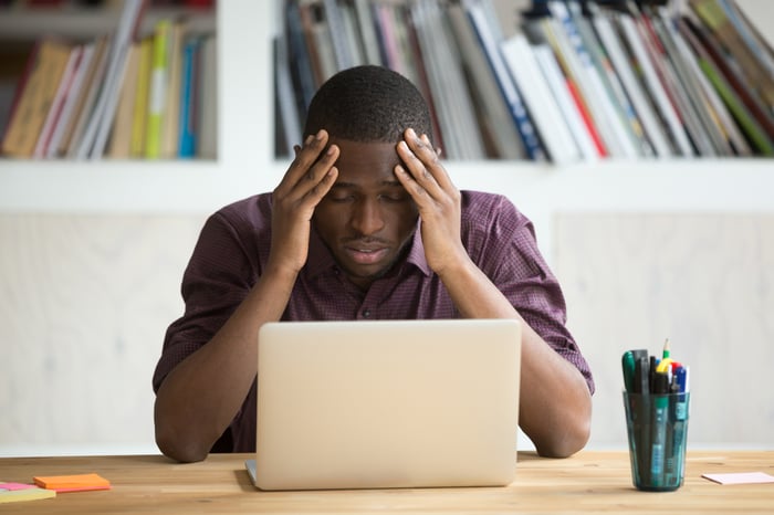 A frustrated investor puts their hands on their head while looking at a computer.