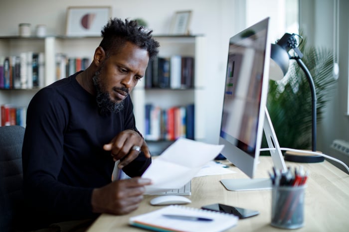 A person at a desk holding and looking at a piece of paper.