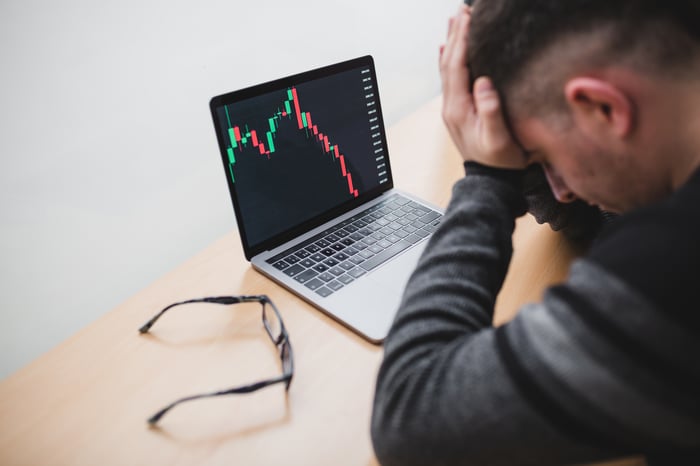 investor with head in hands and laptop showing plunging stock chart in front. 