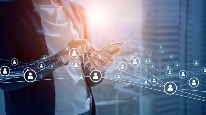 A digital network of icons is displayed around a person using a smartphone.