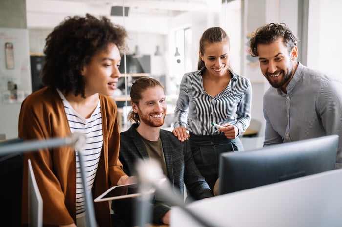 A group of investors gathers around a computer screen.