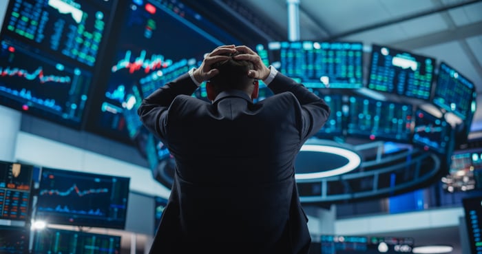 A person in a trading room puts their hands on their head.
