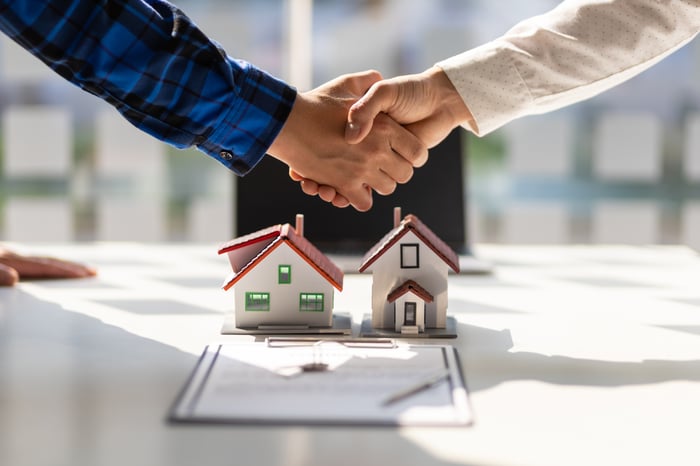 A handshake over a signed document and a house in front of it. 