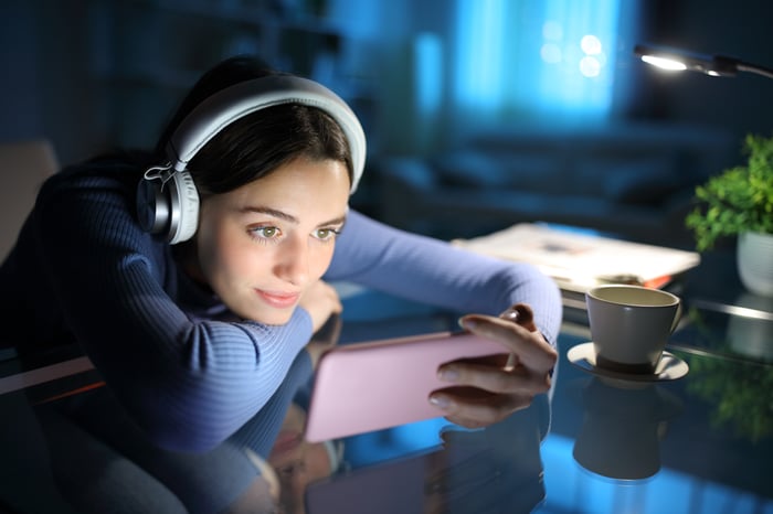 A person looks at phone while wearing headphones. 