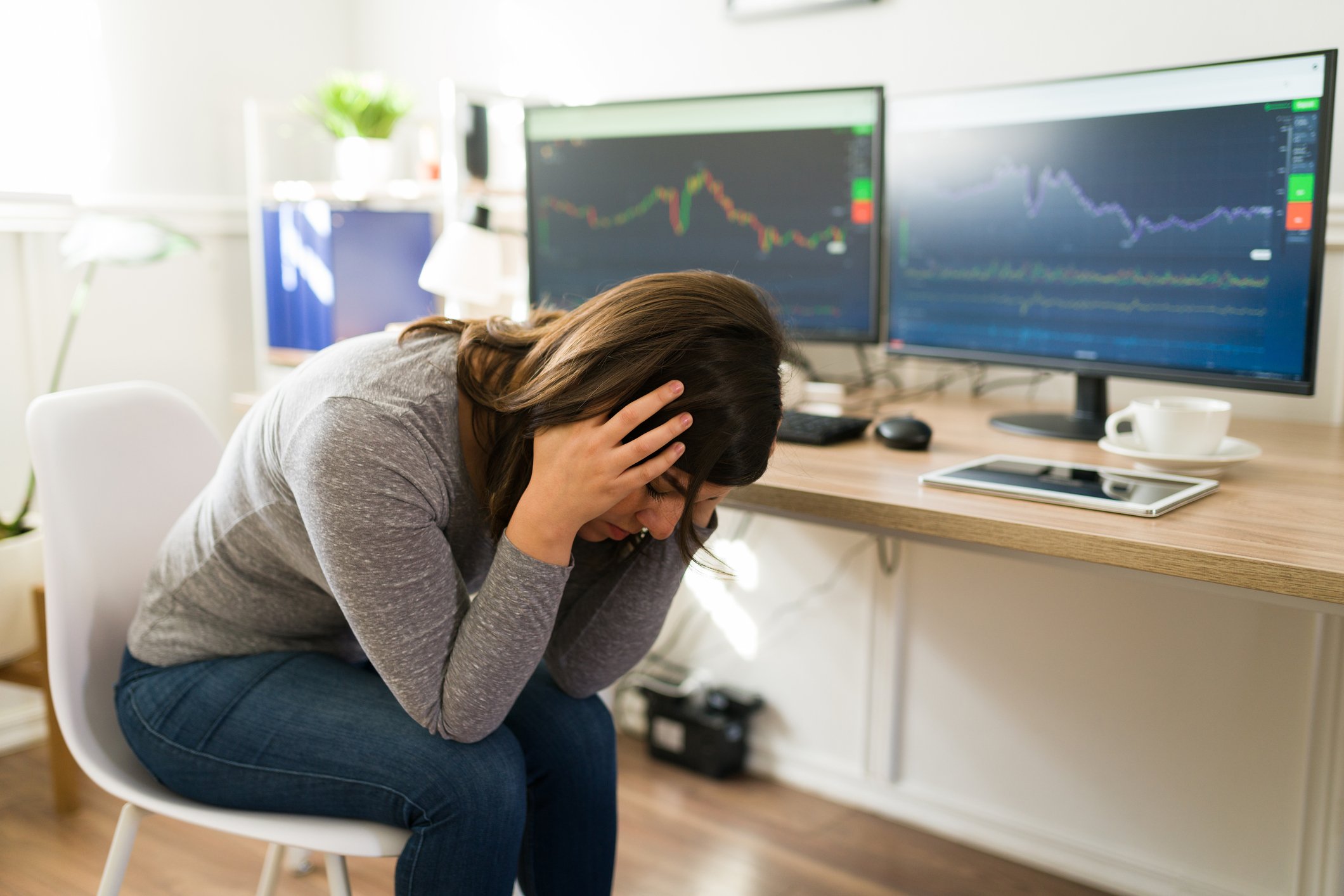 Person seated at a desk with two PC monitors holding head in hands.