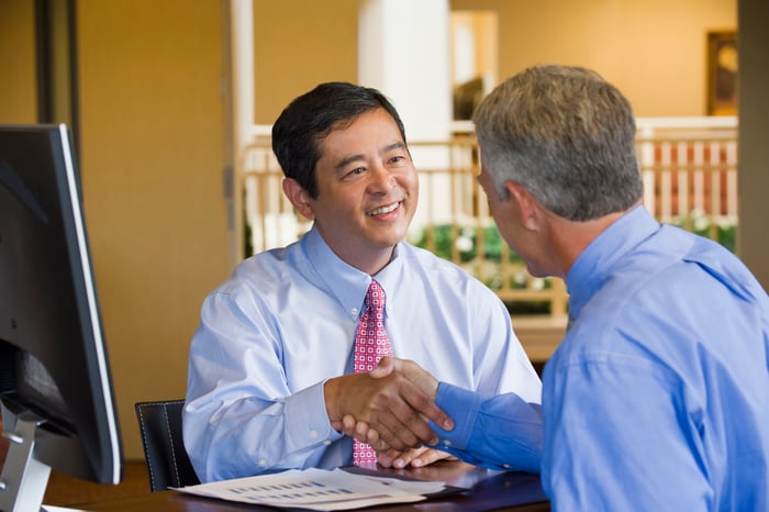 Two people shaking hands at their desk.