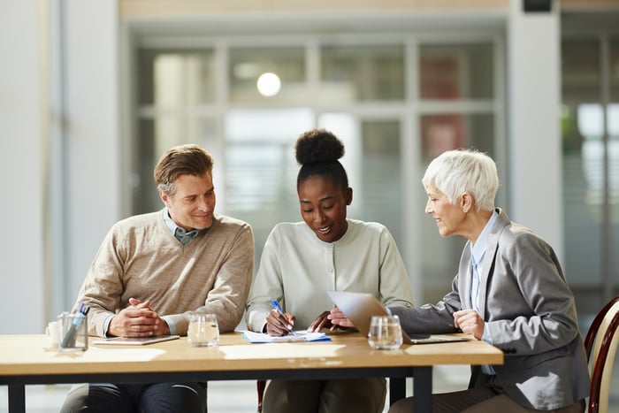 Three professionals are sitting together at a table, reviewing documents and discussing work.