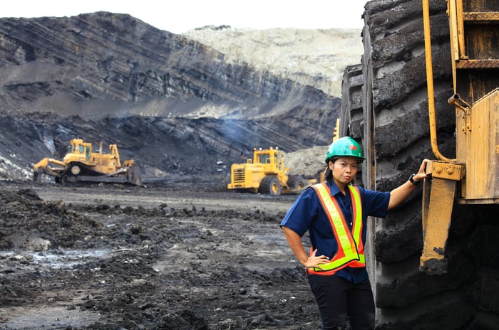 A person in protective gear standing by a giant truck in a mine site.