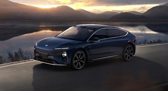 Nio electric sedan on scenic road with sun setting behind mountains in background.